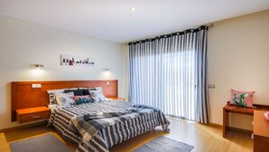 Een slaapkamer met een groot bed, een nachtkastje, een wandlamp, een raam met gordijnen en een cactus decoratie.