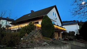 Une maison avec un toit en pente, une cheminée et une véranda décorée de guirlandes lumineuses.