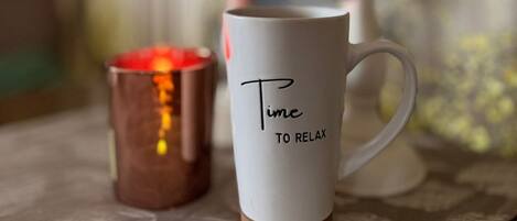 A white mug with 'Time to Relax' text, a copper candle holder, and a decorative candle on a table.