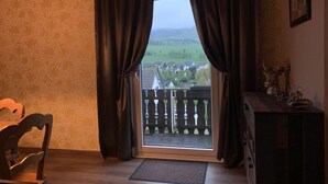 Une pièce avec vue sur un village, visible à travers une fenêtre ornée de rideaux.