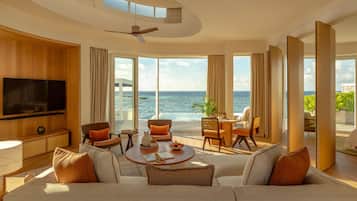 A spacious living room with a large flat-screen TV, comfortable seating, and a view of the ocean.