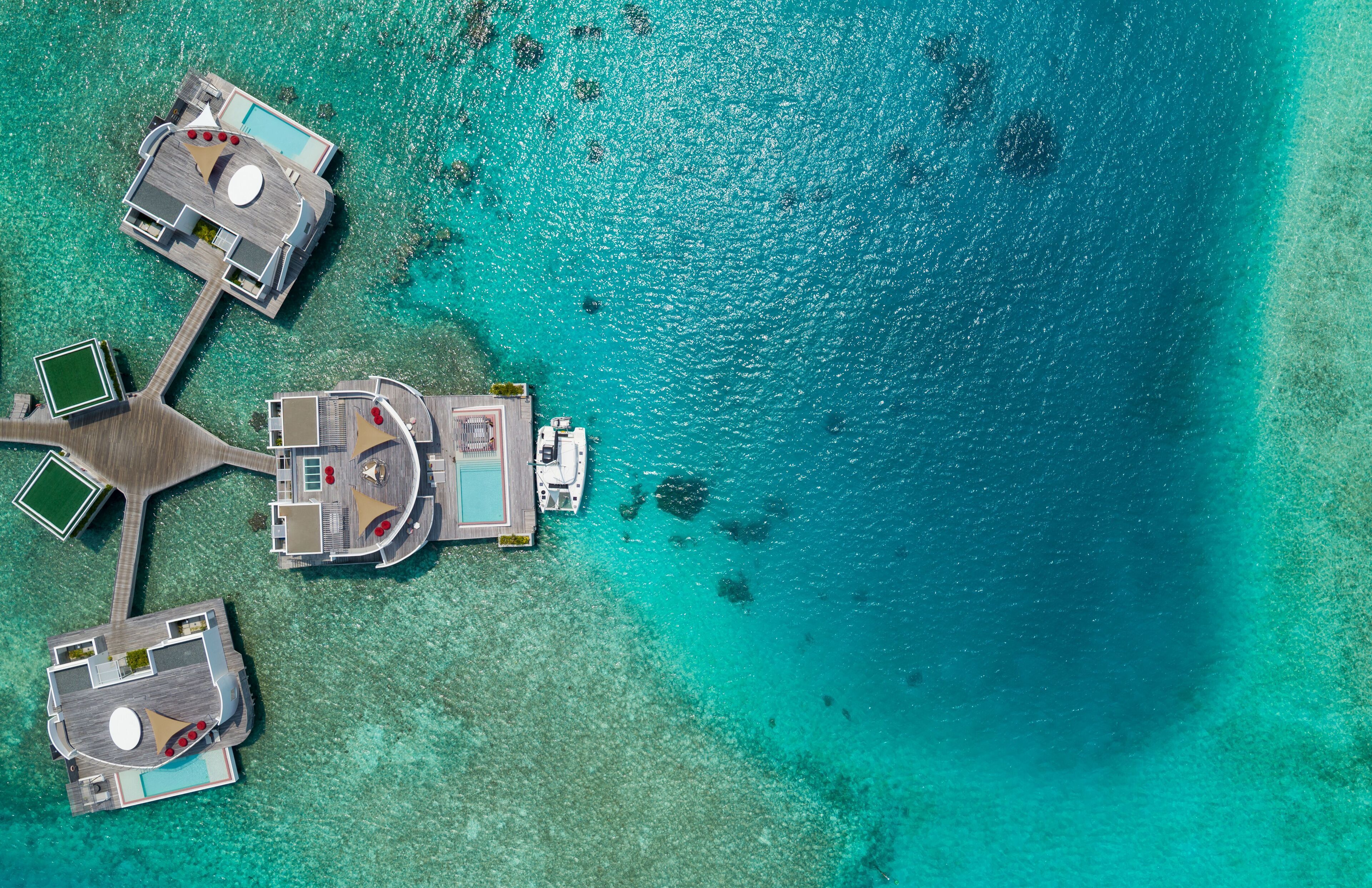 An aerial view of a resort with multiple overwater bungalows connected by walkways, surrounded by turquoise waters.