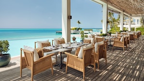 A wooden deck with wicker furniture, a pool, and a view of the ocean. - Jumeirah Olhahali Island  (Olhahali)