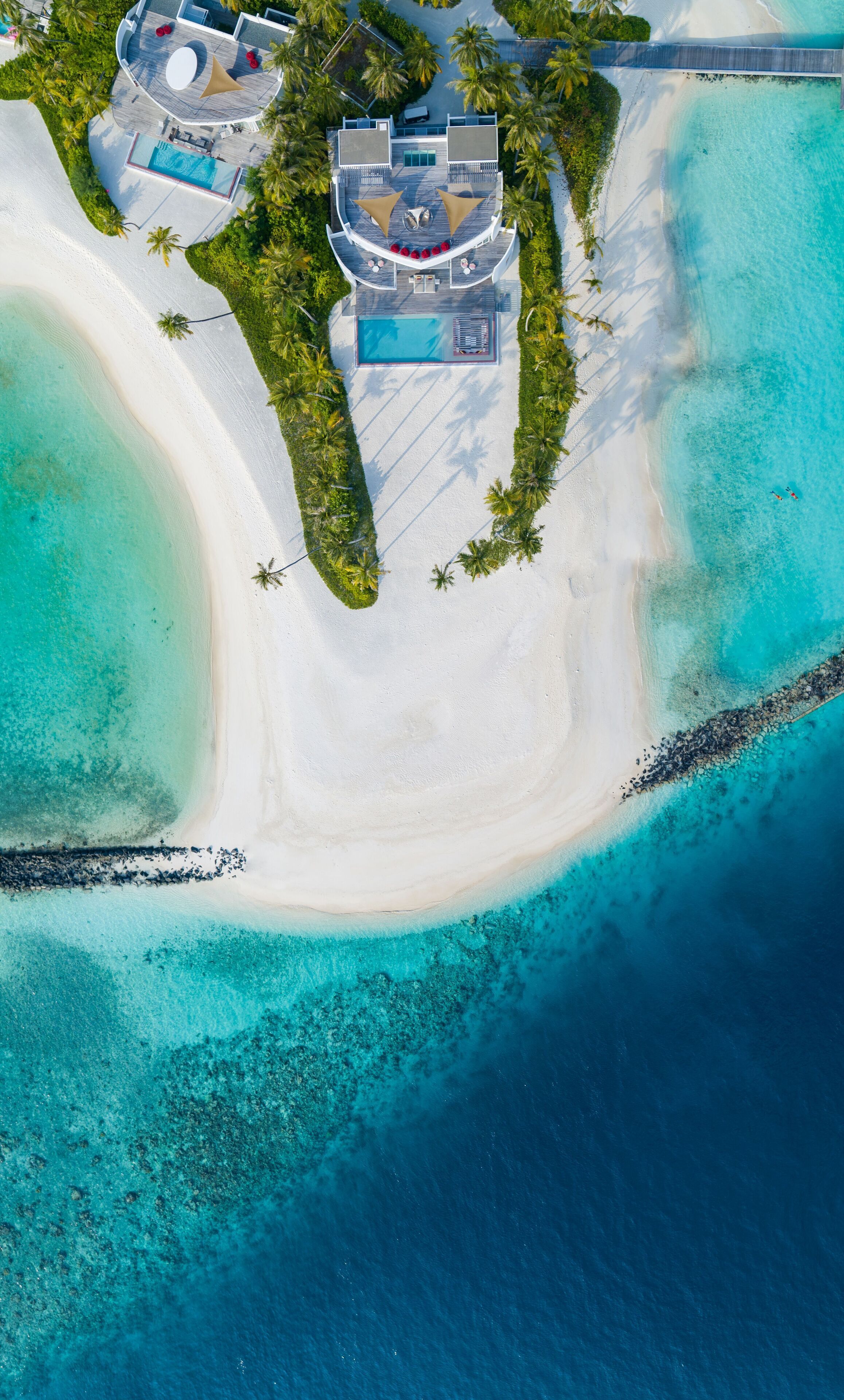 Vista aérea de un complejo turístico con una piscina grande, varias zonas de descanso y una playa.