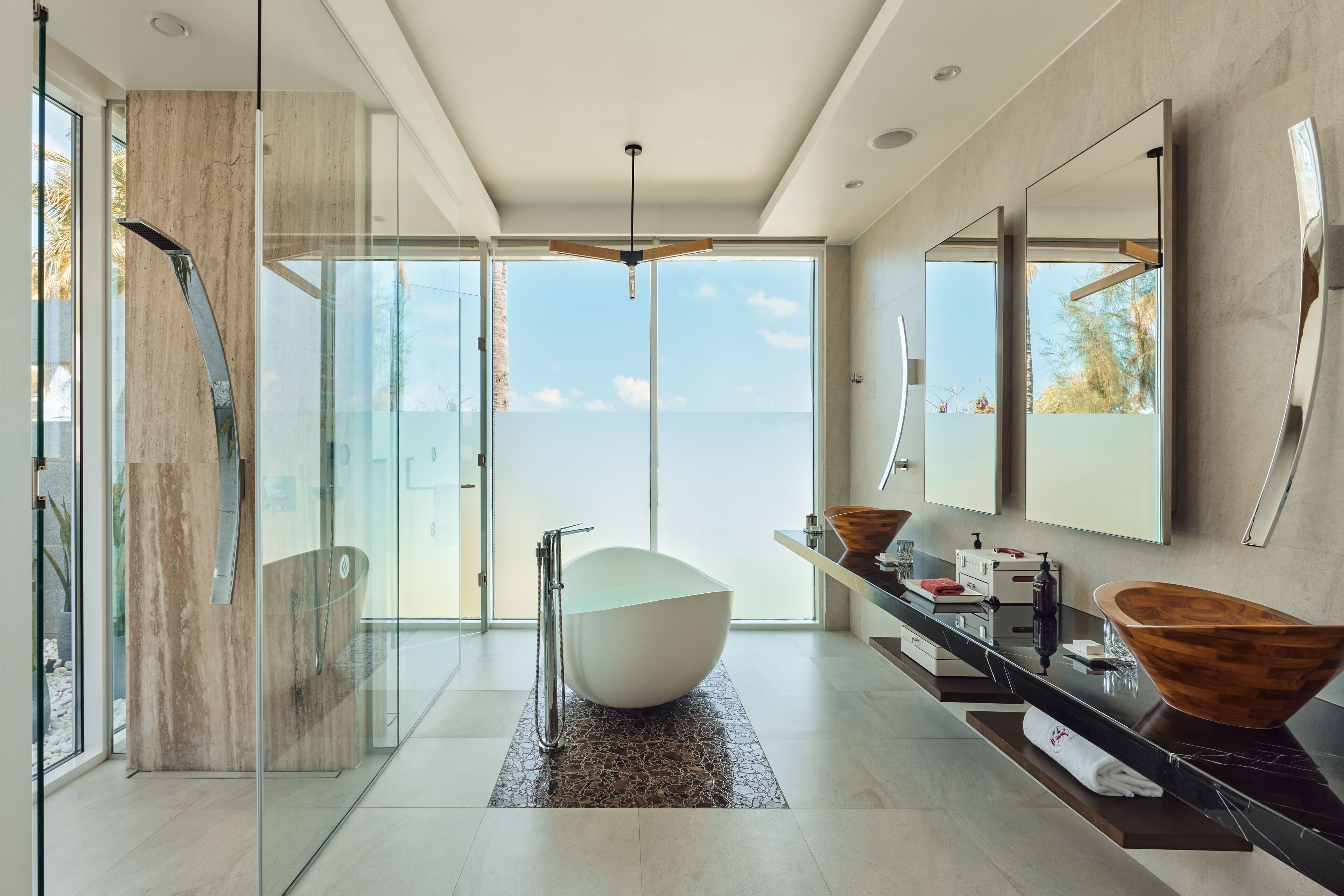 Un baño moderno con una bañera independiente, cabina de ducha con vidrio y espejos amplios.