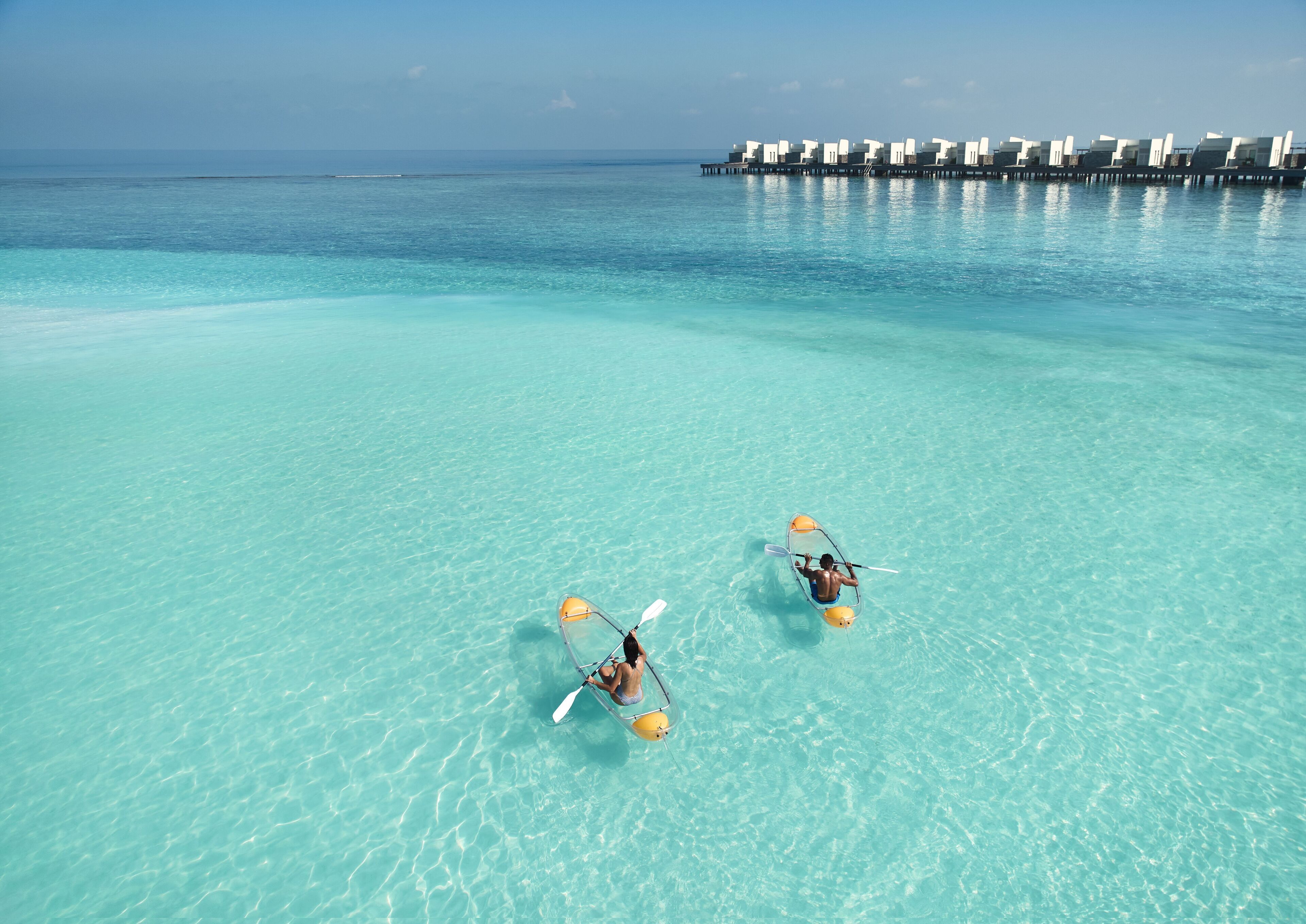 Two kayaks on a clear turquoise sea with overwater bungalows in the background.