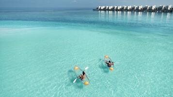 Two kayaks on a clear turquoise sea with overwater bungalows in the background.