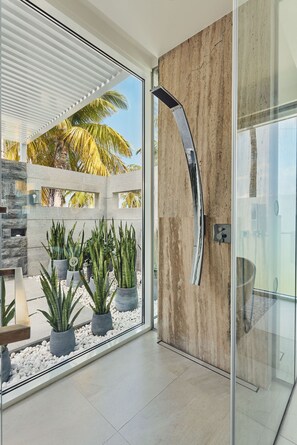 A modern bathroom with a glass shower enclosure, a wooden wall, and a view of palm trees outside. - Jumeirah Olhahali Island  (Olhahali)