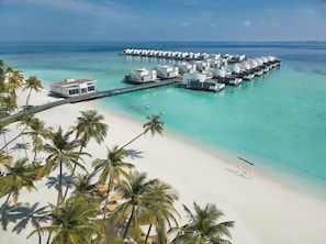 An overwater resort with multiple bungalow-style accommodations connected by walkways to a sandy beach and palm trees. - Jumeirah Olhahali Island  (Olhahali)