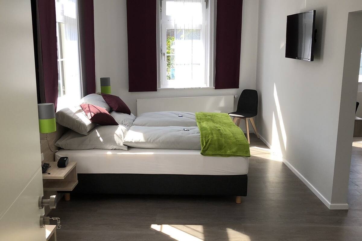 Ein modernes Schlafzimmer mit Bett, Fernseher und Fenster.