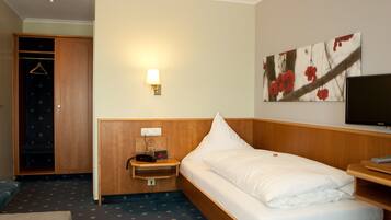 A hotel room with a bed, a TV, a bedside table with a lamp, a wardrobe, and a painting on the wall.