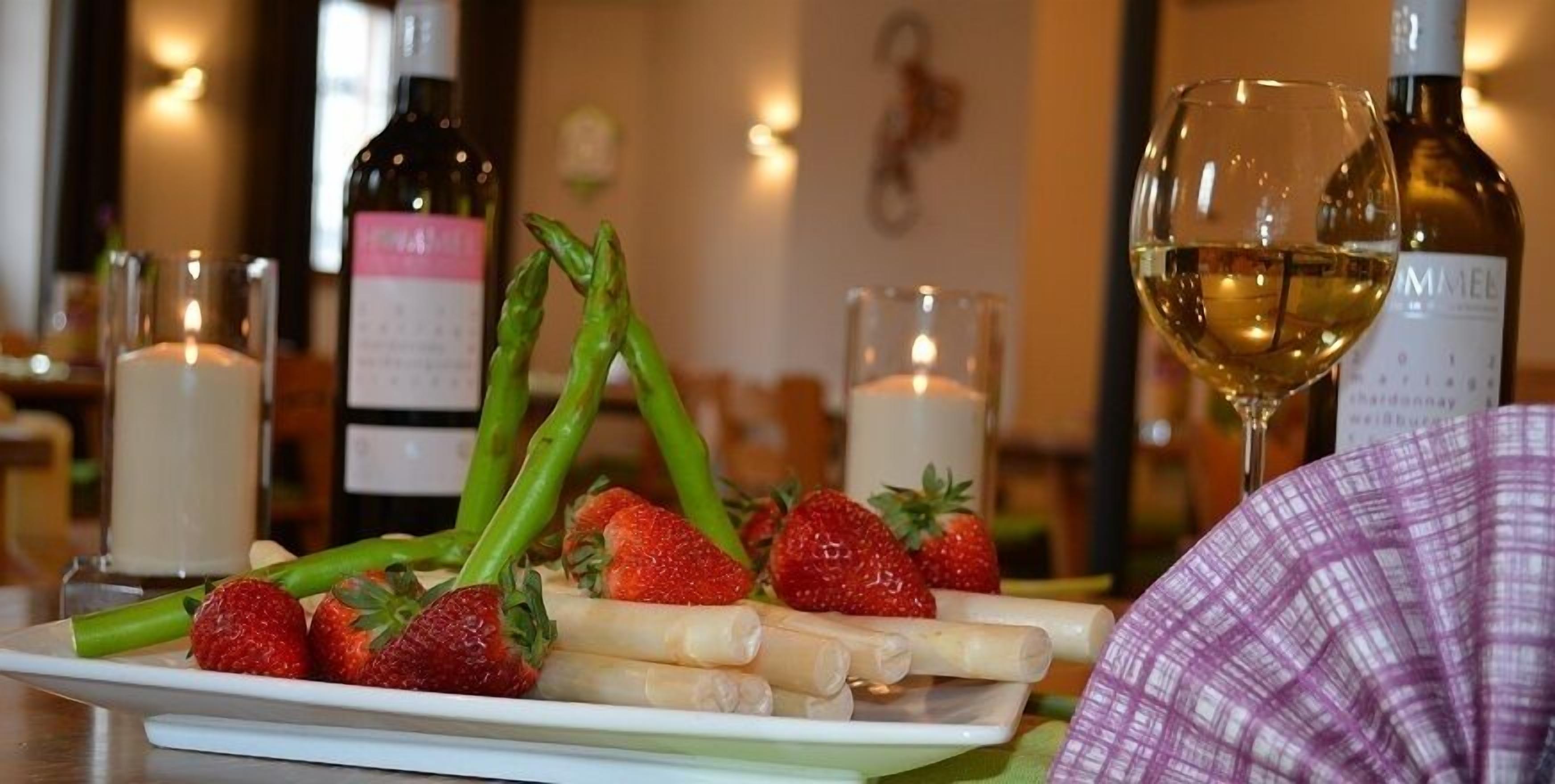 A plate with asparagus and strawberries, a glass of white wine, and candles on a table.