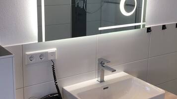 A modern bathroom with a white sink, a mirror with integrated lighting, and a shower area.