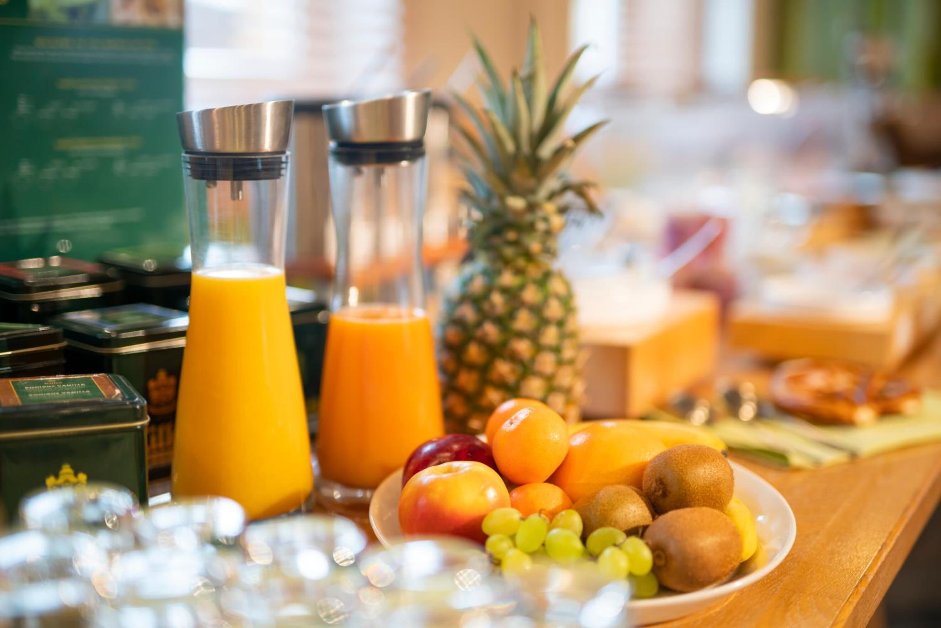 A breakfast buffet with a variety of fruits, a pineapple, and two juice dispensers.