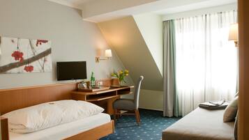 A hotel room with a bed, a desk with a chair, a television, and a window with curtains.