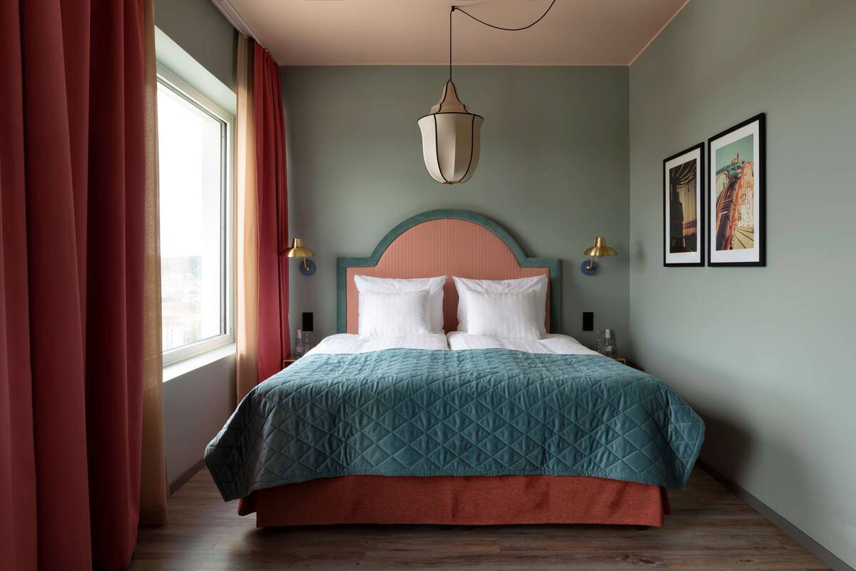 A neatly made bed with a teal quilt, a wooden headboard, and a hanging light fixture.