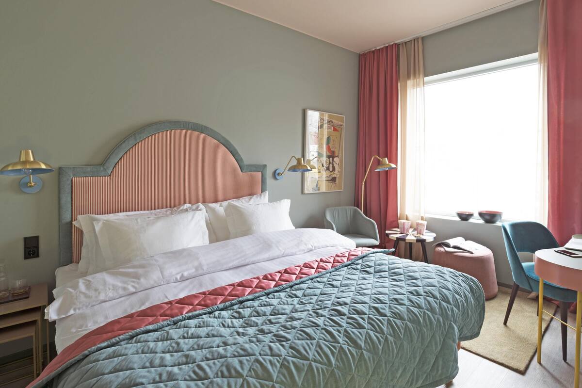 A hotel room with a bed, bedside tables, a desk, a chair, and a window with curtains.