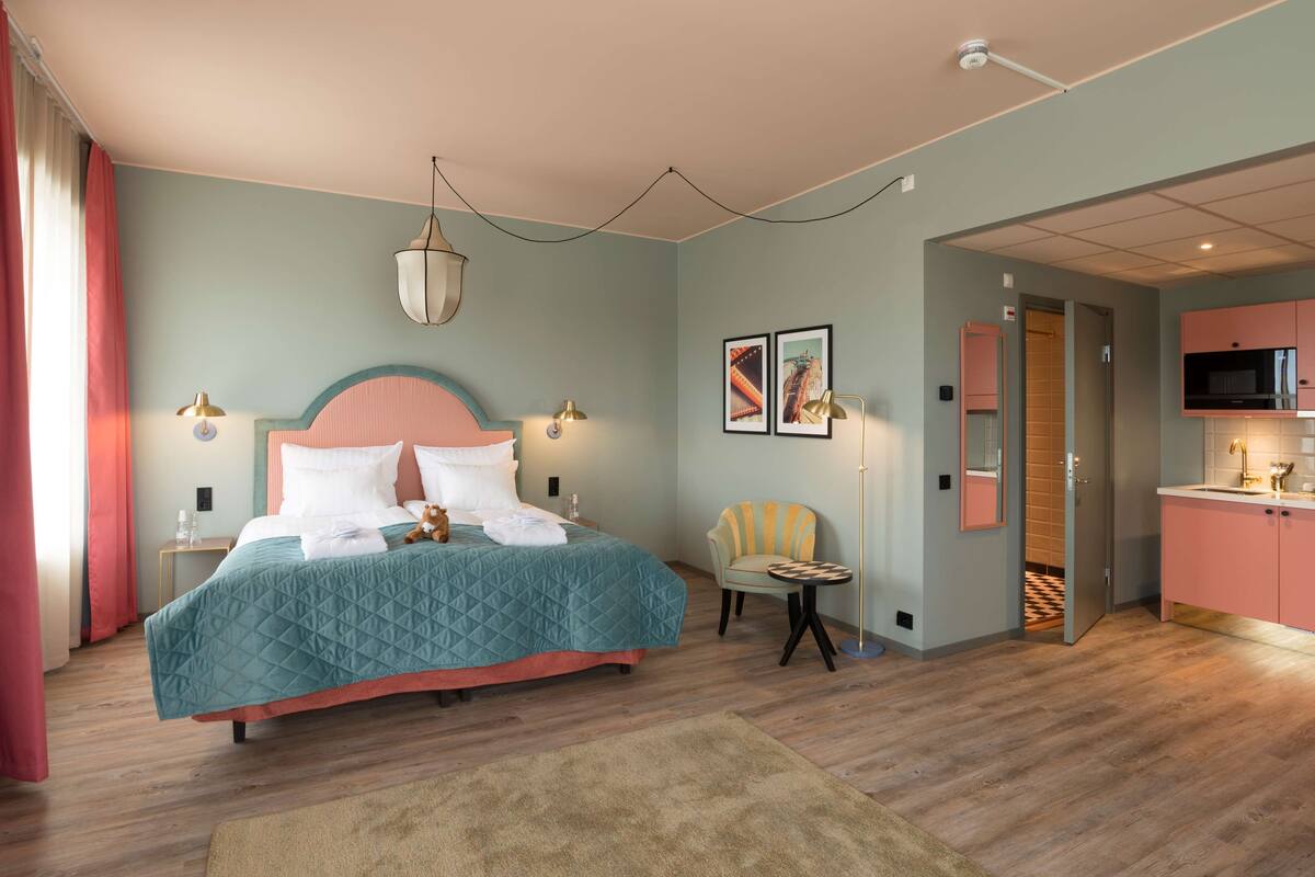 A bedroom with a bed, bedside tables, a chair, a small table, and a door leading to a bathroom.