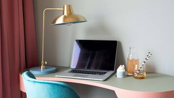 A desk with a laptop, a gold desk lamp, a glass bottle, and a glass with a straw.