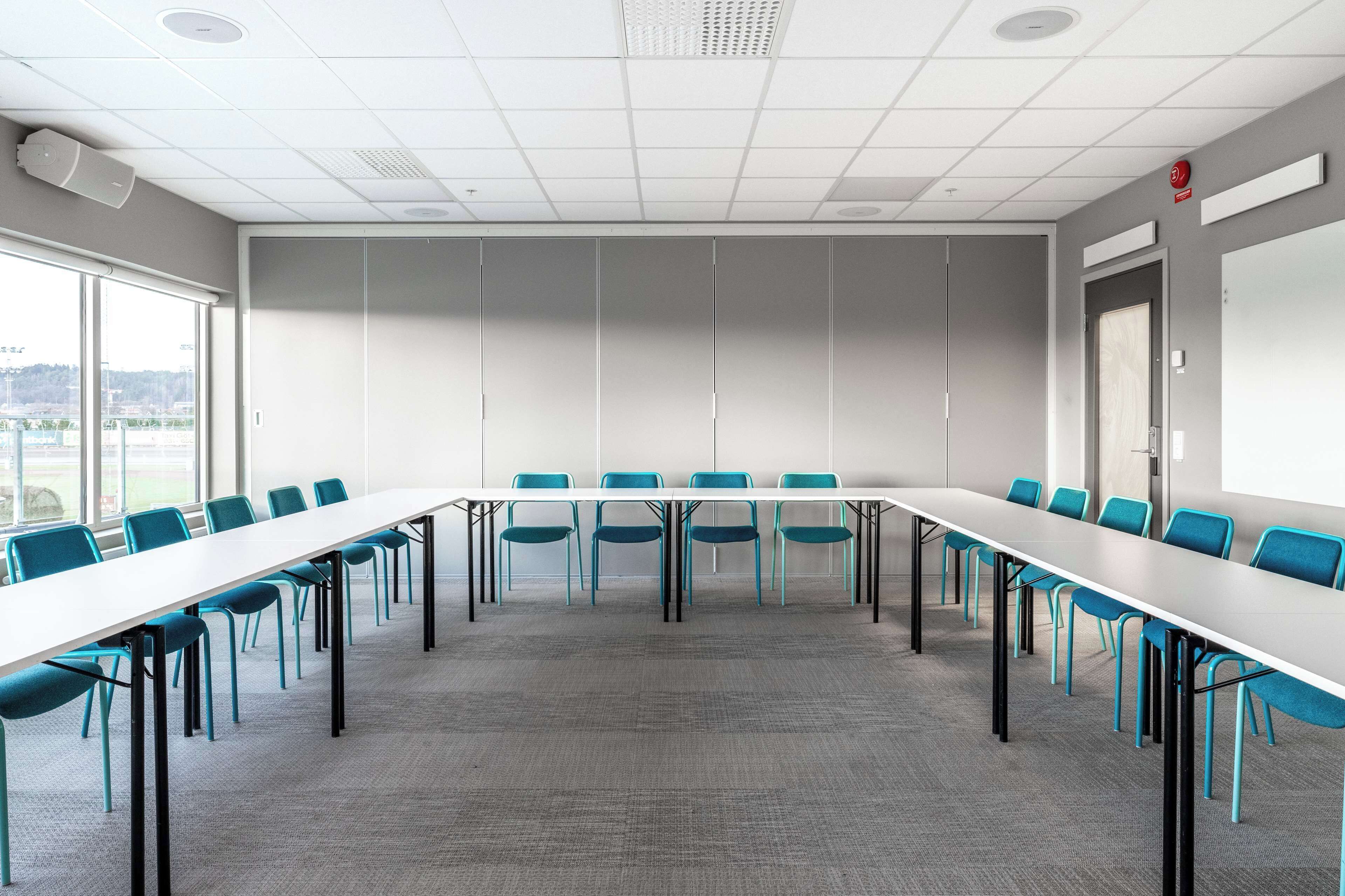 A conference room with a long table and chairs, large windows, and a view of the outdoors.