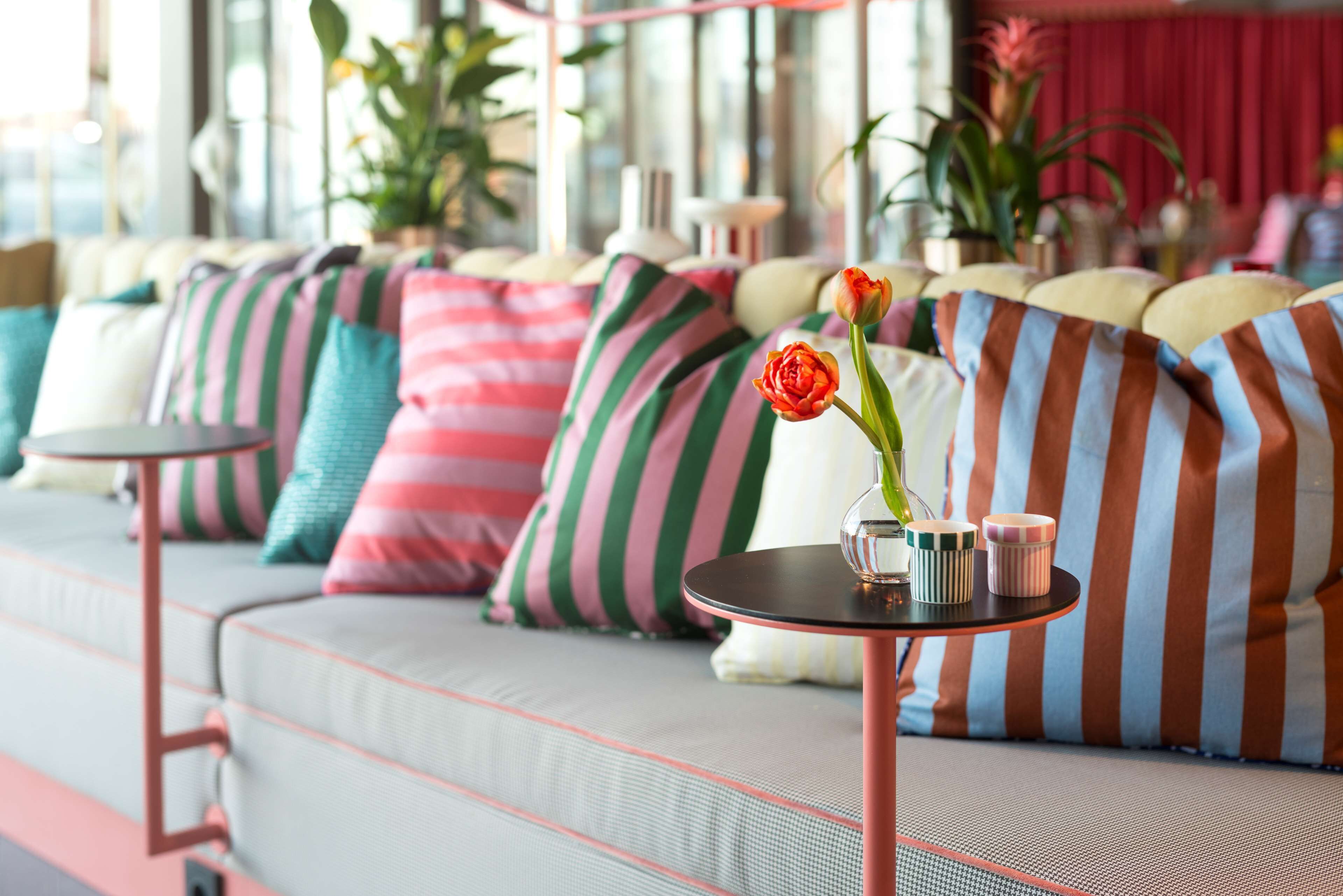 Un salon moderne avec un canapé agrémenté de coussins à rayures, une petite table ronde sur laquelle est posé un vase de fleurs, et un rideau rouge en arrière-plan.