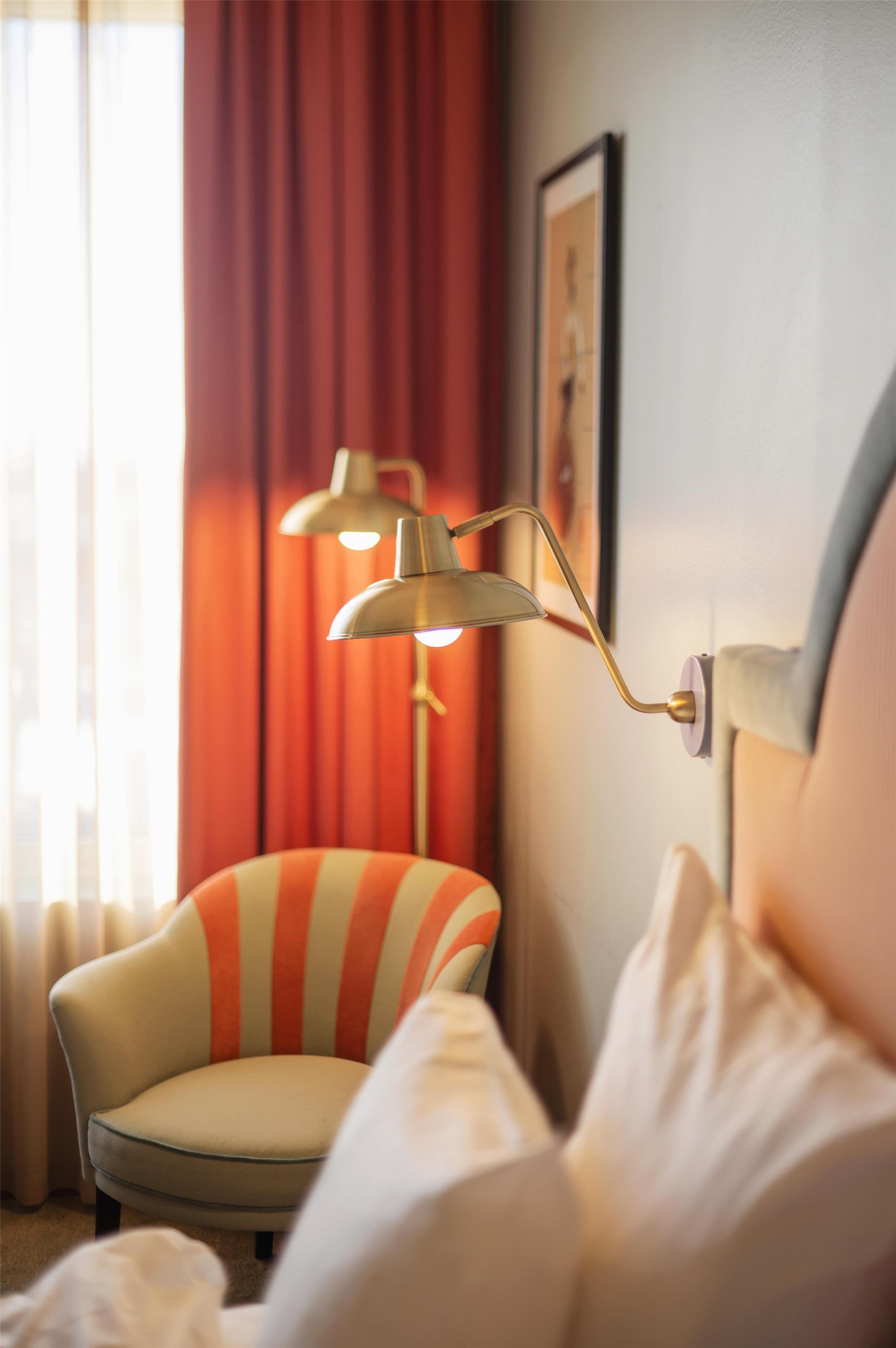 Una habitación de hotel con un sillón a rayas, una lámpara de pared y un cuadro en la pared.