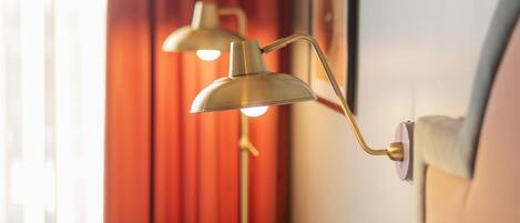 A hotel room with a striped armchair, a wall-mounted lamp, and a framed picture on the wall.