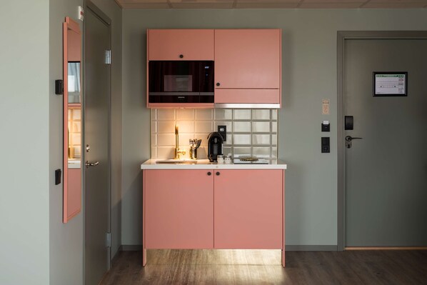 A modern kitchen with pink cabinets, a microwave, and a coffee machine. - Best Western Plus Aby Hotel (Mölndal)