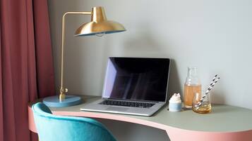 Um laptop sobre uma mesa com uma luminária dourada, uma garrafa de vidro e um copo com canudo.