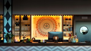 Een bar met een grote klok, planken vol flessen en glazen, en twee rode barkrukken.