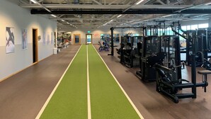 Een sportschool met een groene loopbaan, trainingsapparatuur en posters aan de muren.