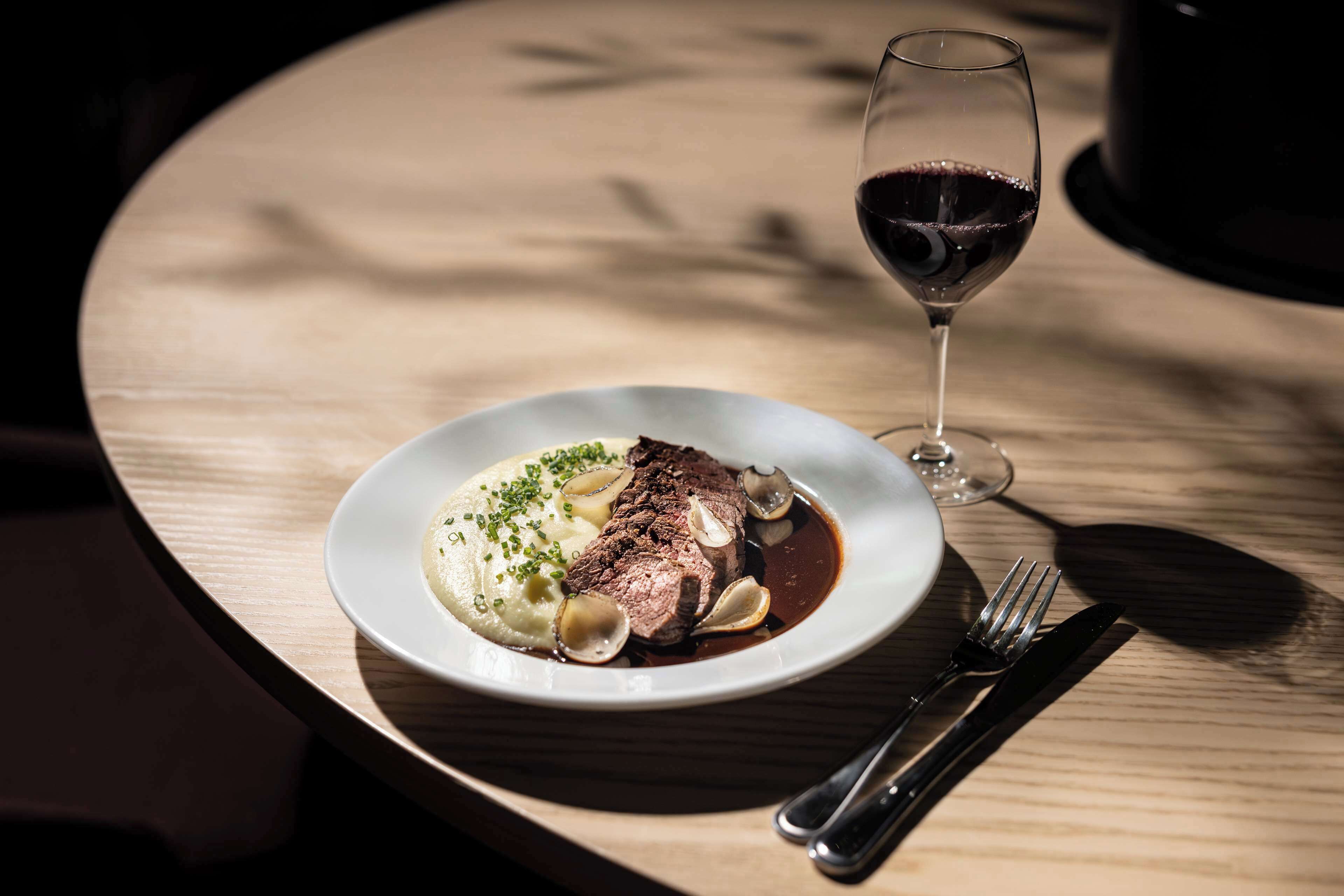 Une assiette de nourriture accompagnée d’un verre de vin rouge, le tout posé sur une table en bois.