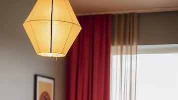 A hotel room with a bed, a chair, a lamp, a window with curtains, and a framed picture on the wall.