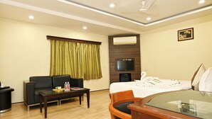 A hotel room with a sofa, a dining table with chairs, a TV mounted on the wall, and a bed with a white bedspread. - Hotel Simran (Raipur)