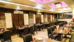A restaurant with multiple tables and chairs, air conditioning units, and decorative elements on the walls. - Hotel Simran (Raipur)