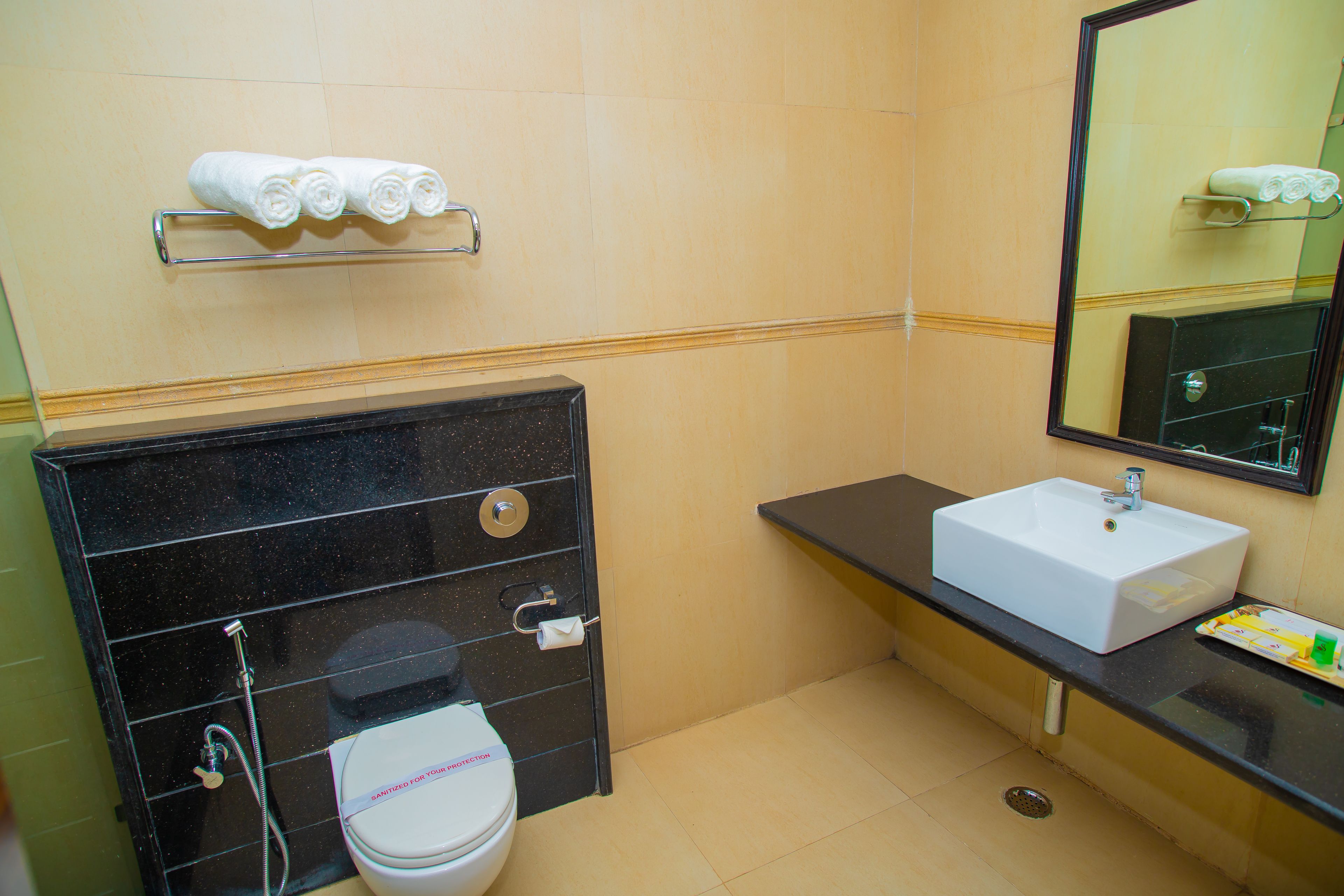 A bathroom with a toilet, sink, and mirror. There are towels on a rack above the sink.