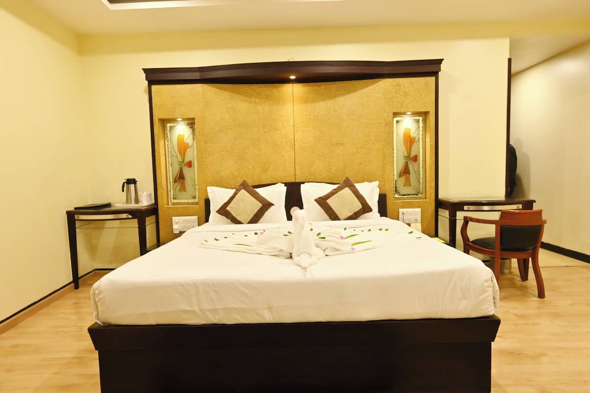 A hotel room with a large bed, a desk, a chair, and a mirror.