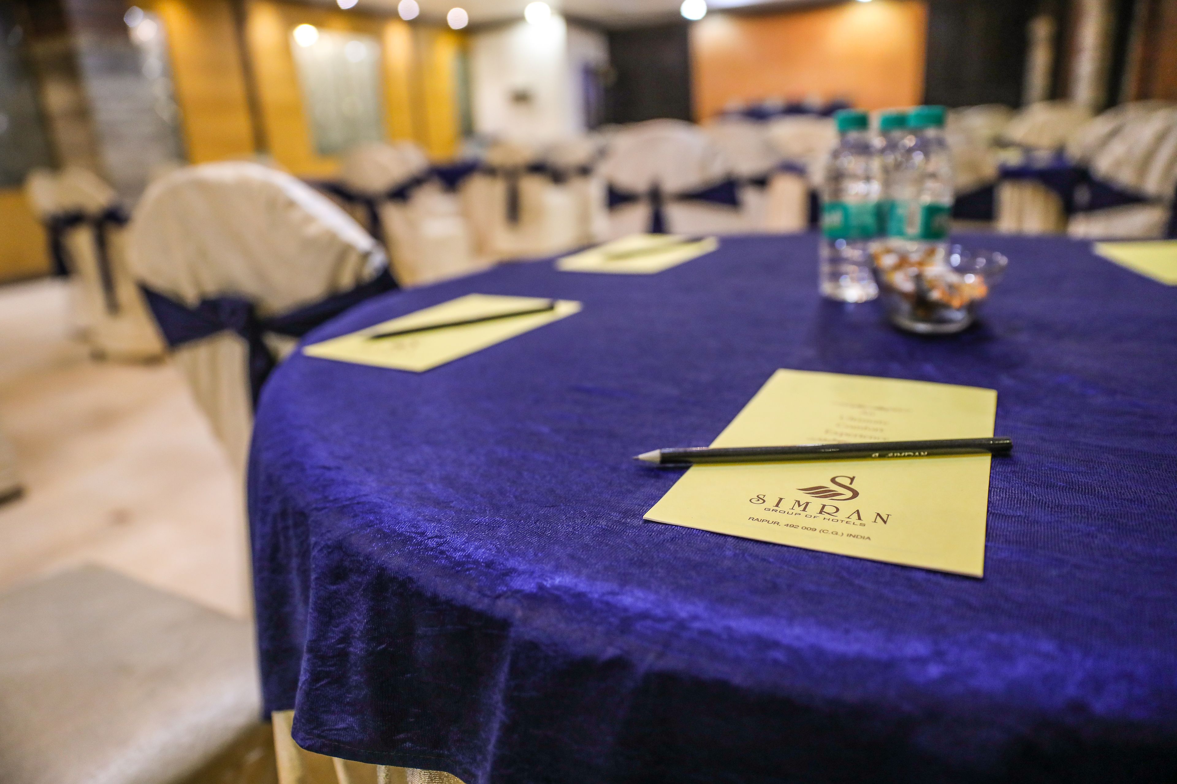 A conference table with a blue tablecloth, a pen, a notepad, and a bottle of water.