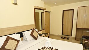 A hotel room with a neatly made bed, a mirror, a wardrobe, and a desk with a telephone. - Hotel Simran (Raipur)