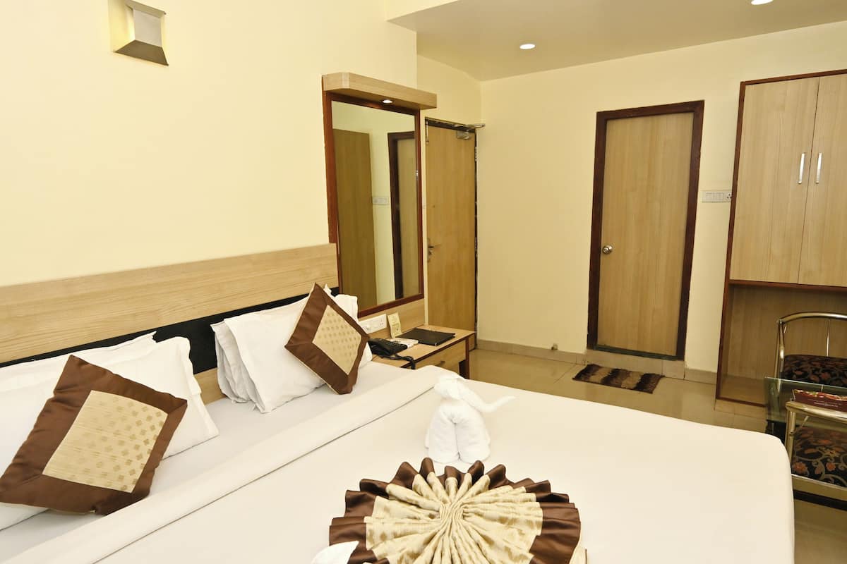 A hotel room with a neatly made bed, a mirror, a wardrobe, and a desk with a telephone.