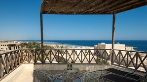 Un balcón con sillas de mimbre, una mesita redonda con botellas y vista a la playa y al océano.
