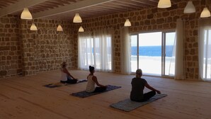Un estudio de yoga con paredes de piedra, pisos de madera y amplios ventanales con vistas a la playa.