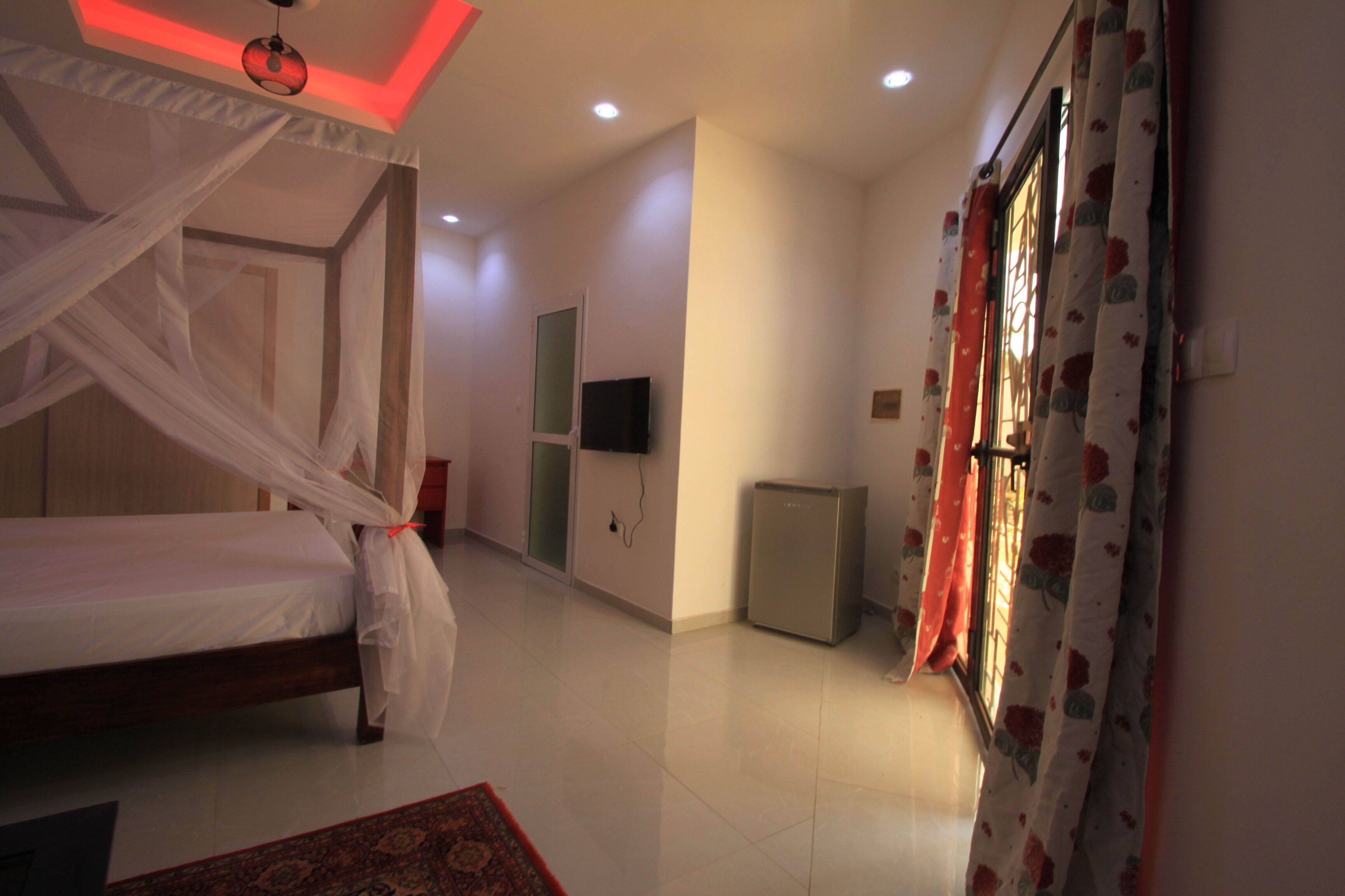 Un dormitorio con cama, televisión, refrigerador y cortinas.
