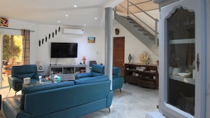 A spacious living room with a large flat-screen TV, a staircase, and a dining area with a table and chairs. - Superb villa with pool, 5 minutes from Saly (Ngaparou)