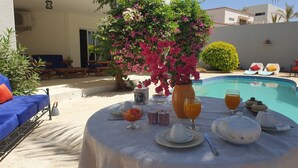 A poolside breakfast setup with a table, fruit bowl, drinks, and a decorative vase. - Superb villa with pool, 5 minutes from Saly (Ngaparou)