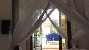 A room with a bed, a window with sheer curtains, and a view of an outdoor area with a blue chair and a gate. - Superb villa with pool, 5 minutes from Saly (Ngaparou)