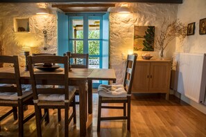 Un coin repas rustique, avec des meubles en bois, un mur en pierre et une porte bleue donnant sur l’extérieur.