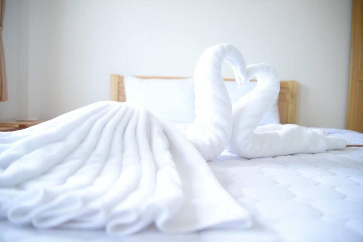 A bed with a white blanket and a towel arranged in a heart shape.