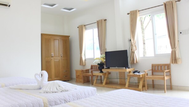 Quarto de hotel com duas camas, uma escrivaninha com televisão, mobiliário de madeira e janelas amplas com cortinas.