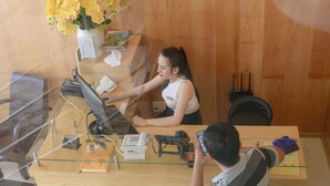 Bancada de recepção com computador, telefone e um vaso de flores amarelas.